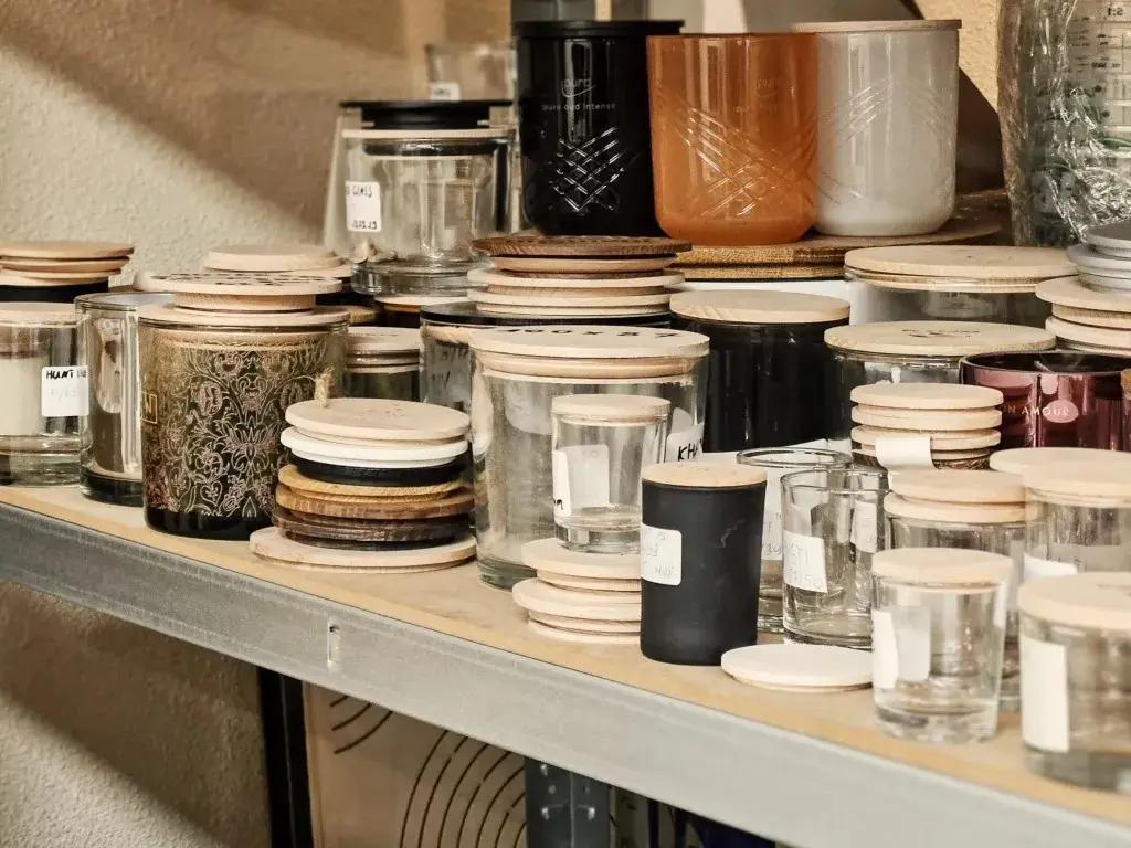 Regał z akcesoriami do produkcji świec: szklane słoiki oraz dopasowane do nich wieczka drewniane i drewniane pokrywki do świec w różnych rozmiarach,A rack with candle-making supplies: glass jars with matching wooden lids and wooden candle lids in various sizes
