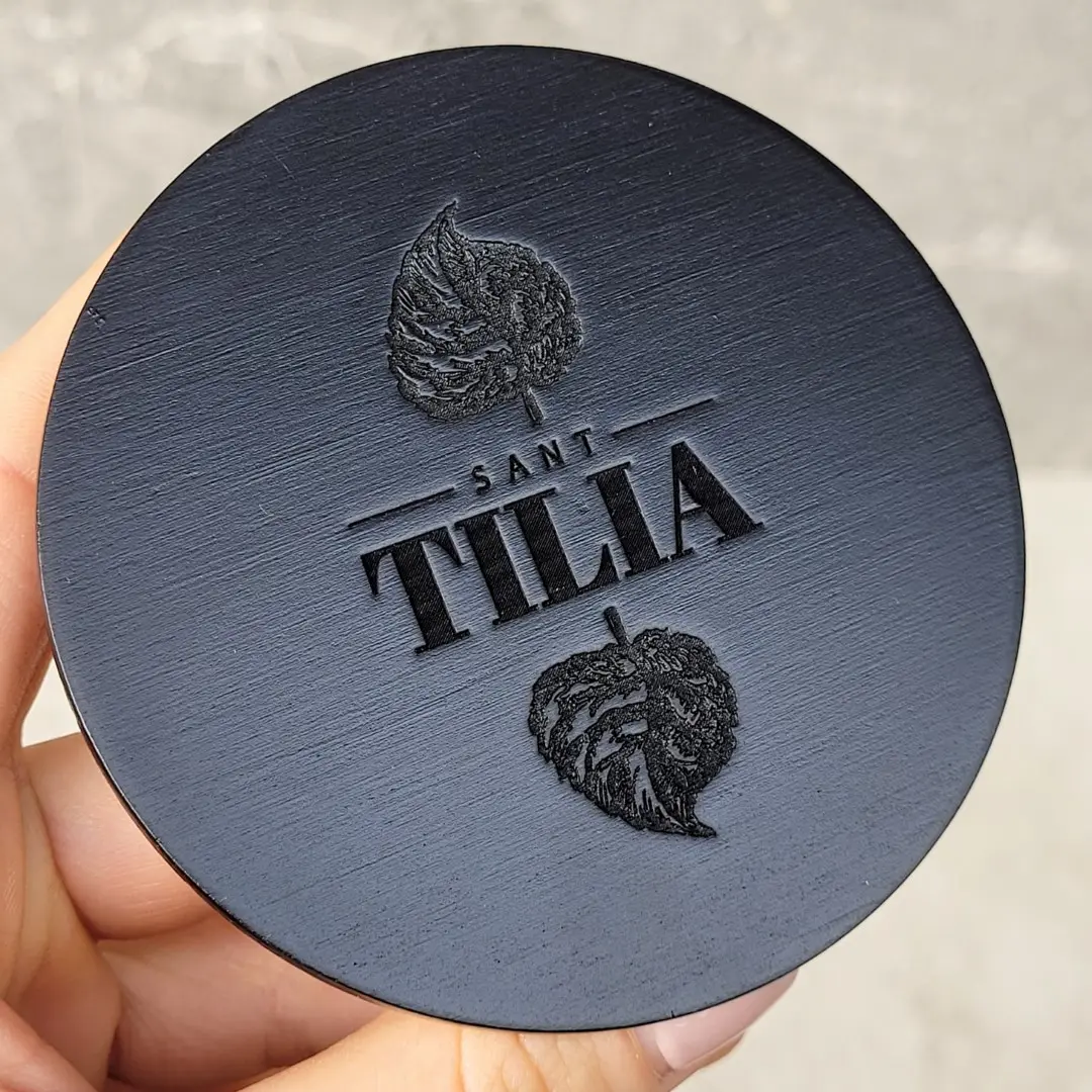 Czarna matowa pokrywka z eleganckim, głębokim grawerem logo – personalizowane drewniane wieczka do świec,A matte black lid with an elegant, deep-engraved logo – personalized wooden candle lids